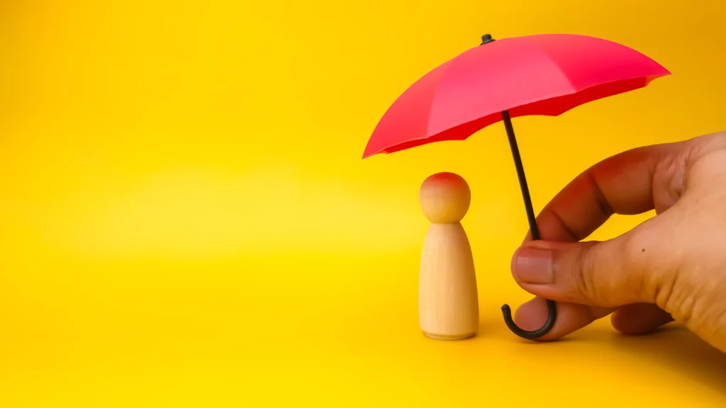 Hand holding red umbrella with peg doll on a yellow background.Insurance cover concept.